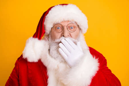 Photo of astonished santa claus impressed stare stupor x-mas atmosphere fairy magic close cover face lips hand wear red costume isolated over bright shine yellow color backgroundの写真素材
