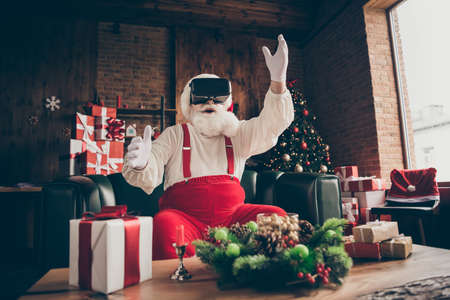 Photo of shocked addicted grey beard santa claus sit couch player play 3d simulation game use goggles wear red cap headwear in house indoors x-mas christmas decorationの写真素材