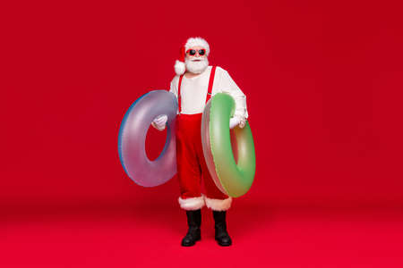 Full length body size view of his he nice handsome cheerful bearded fat Santa carrying rubber circles rest relax pool party celebrate isolated bright vivid shine vibrant red color backgroundの写真素材