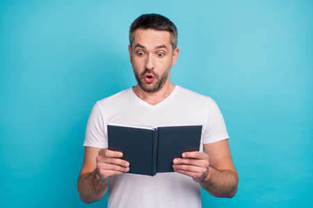 Close-up portrait of his he nice attractive cheerful cheery amazed bearded guy reading interesting book isolated over bright vivid shine vibrant blue color backgroundの写真素材