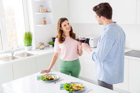 Portrait of his he her she two nice attractive cheerful cheery spouses spending romantic day eating domestic dish restaurant clinking wine in light white interior kitchen house apartmentの写真素材