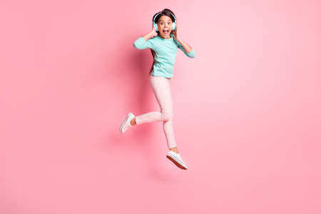 Full length body size photo of crazy little hispanic girl jumping up shouting wearing earphones isolated on pink color backgroundの写真素材