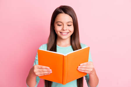 Photo of lovely cute little latin lady long hairstyle hands hold orange classbook cheerful toothy white smile read wear turquoise teal sweatshirt isolated pink color backgroundの写真素材