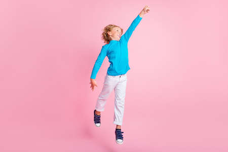 Full length photo of small boy jump raise fist wear blue turtleneck pants sneakers isolated pastel pink color backgroundの写真素材