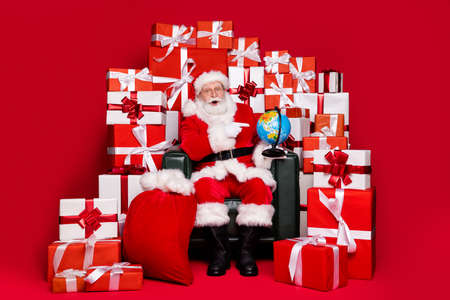 Full length body size view handsome amazed fat Santa sit in chair pile stack gifts sending order finding country map rout destination shipping isolated bright vivid shine vibrant red color backgroundの写真素材