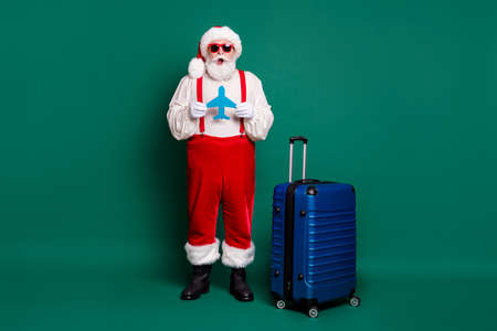Full length body size view of nice handsome funky amazed bearded overweight fat Santa grandfather holding in hands paper plane shape card air flight fly departure sale isolated green color backgroundの写真素材