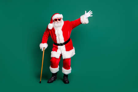 Full length body size view of his he nice attractive cheery childish playful funky Santa leaning on cane having fun celebration festal day Eve Noel isolated over green color backgroundの写真素材