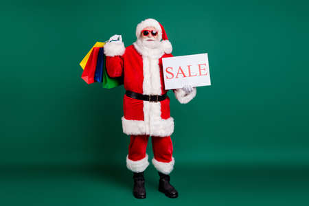 Full length body size view of his he nice fat cheery confident Santa father carrying gifts presents surprise order bargain holding in hand sale promo card isolated over green color backgroundの写真素材