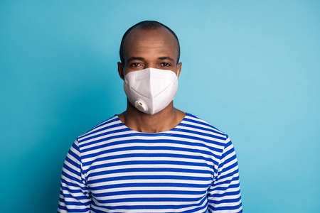 Portrait of charismatic dark skin guy travel trip on covid infection quarantine stay safe look in camera wear striped sailor vest white medical mask isolated over blue color backgroundの写真素材