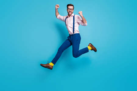 Full body profile photo of handsome man jump high up running competition work worker raise fists first place winner wear specs shirt suspenders pants boots isolated blue color backgroundの写真素材