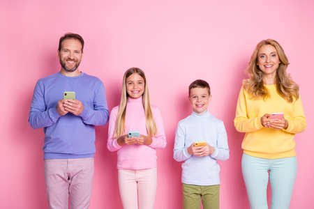 Photo of positive mom dad and little kids hold digital cellphone isolated over pastel color backgroundの写真素材