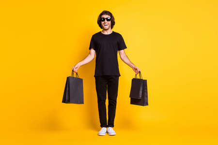Full body size photo of young man posing hold shop packages wear black t-shirt pants white sneakers...