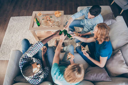 Top above high angle view photo of positive four men meeting celebrate college holiday start eat pizza clink cheers toast beer bottle sit divan in house indoorsの写真素材
