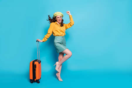 Full size photo of ecstatic girl win weekend lottery tour raise fists scream hold suitcase wear style stylish trendy yellow blouse stilettos isolated over blue color backgroundの写真素材