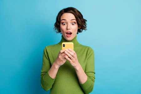 Portrait of astonished blogger girl use smartphone read incredible social network information impressed wear good look pullover isolated over blue color backgroundの写真素材