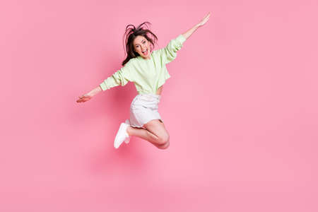 Full size profile photo of attractive funny lady jumping high up spread arms like wings flying wear casual crop pullover naked belly skirt shoes isolated pink pastel color backgroundの写真素材