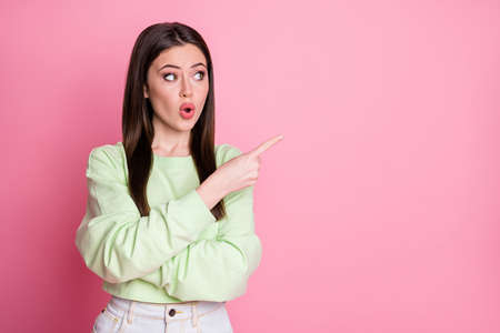 Photo of attractive shocked lady directing finger side empty space showing cool sale prices shopping season wear casual green crop sweatshirt pullover isolated pink color backgroundの写真素材