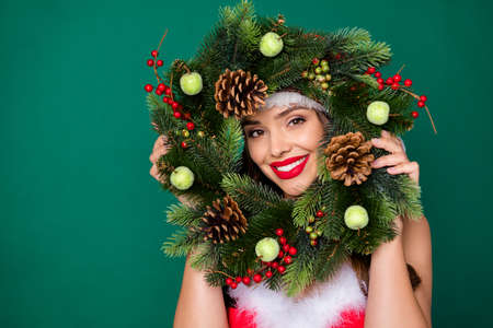 Photo of attractive lady look through newyear season circle wreath christmas tree door house entrance decor tradition good mood wear x-mas snow girl costume isolated green color backgroundの写真素材
