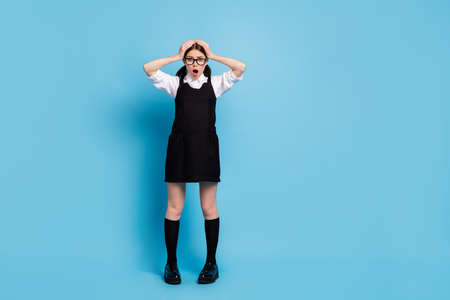 Full length photo of astonished girl touch hands head see unexpected graduate exam schedule information impressed wear uniform overall isolated over blue color backgroundの写真素材