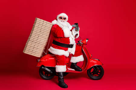 Full length profile photo of retired grandfather retro scooter pizza box hold credit card contactless serve client terminal wear x-mas costume coat sunglass cap isolated red color backgroundの写真素材
