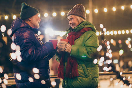 Photo of two people pensioner couple hold mugs drink eggnog comfortable cheerful smile newyear...