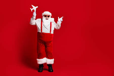 Full length body size view of his he attractive cheerful cheery fat Santa holding in hands paper plane showing copy space isolated bright vivid shine vibrant red burgundy maroon color backgroundの写真素材