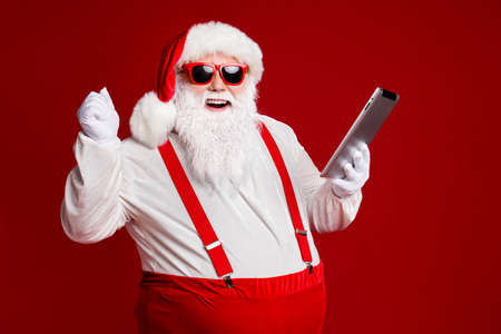 Portrait of his he attractive cheerful cheery lucky fat white-haired Santa using gadget ebook having fun fast speed isolated bright vivid shine vibrant red burgundy maroon color backgroundの写真素材