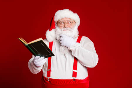 Portrait of his he attractive minded fat white-haired Santa reading book overthinking creating Eve...