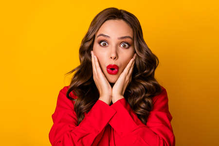 Photo of attractive funky curly lady hold hands on cheeks open mouth crazy facial expression unbelievable news wear red office shirt isolated bright yellow color backgroundの写真素材