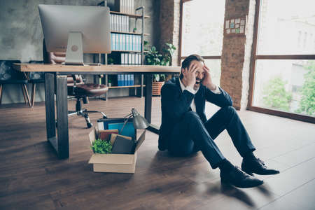 Photo of laid off dismissed sad worker mature guy fail fired agent lost job packed belongings box financial crisis sit floor wooden parquet hopeless cry yell workstation office indoorsの写真素材