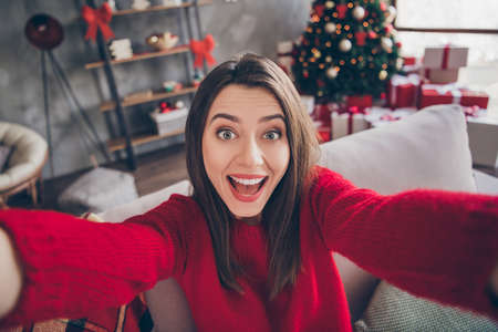 Photo of excited girl make selfie sitting on couch in house indoors with x-mas christmas newyear decorationの写真素材