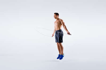 Full length photo of handsone sporty guy using skipping rope to train his perfect body isolated over...