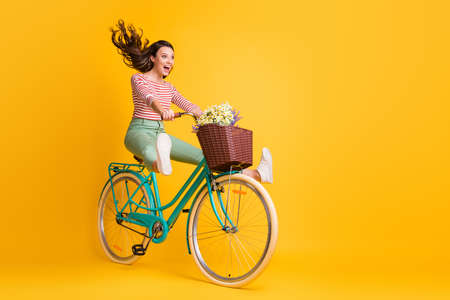 Full length body size photo of funny girl shouting riding bicycle keeping legs up isolated on vivid yellow color backgroundの写真素材