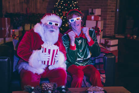 Photo portrait of santa claus and elf in anticipation holding popcorn watching movie on sofa in 3d...