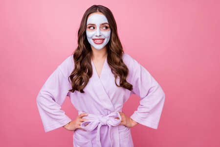 Photo portrait of pretty girl with facial mask long brown wavy hair looking at side keeping hands on waist smiling isolated on pink color backgroundの写真素材