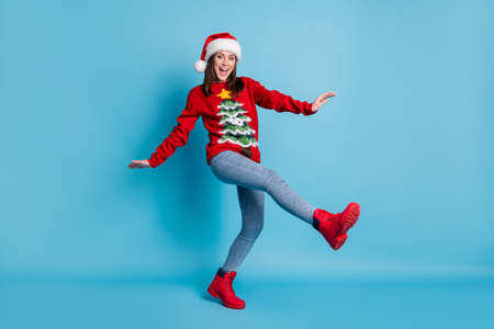 Full body size photo of charming pretty lady raise hands leg dance open mouth wear santa x-mas headwear red ornamented pullover boots jeans isolated blue color backgroundの写真素材