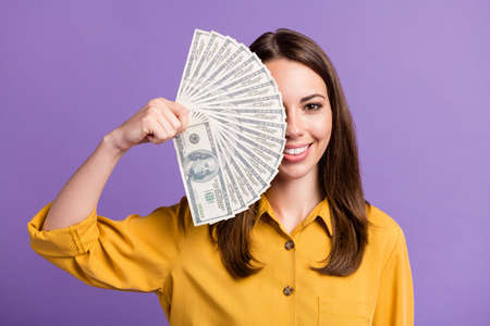 Photo of charming young lady hold fan cash cover hide eye wear yellow shirt isolated purple color...