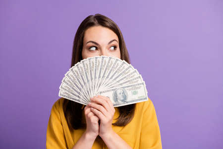 Photo of cute young lady hold fan cash look side empty space cover face wear yellow shirt isolated...