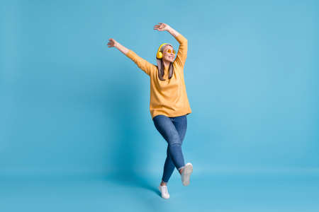 Full body size photo of attractive careless old dancer lady listen music earphones hands waving above head walking street wear sunglass yellow jumper jeans vivid blue color backgroundの写真素材