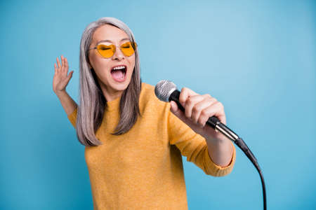 Close-up headshot photo of charming lovely singer old lady holding microphone open mouth close eyes...