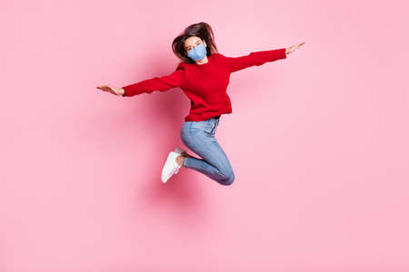 Full length portrait of girl jumping high wearing mask casual clothes keeping hands like plane...