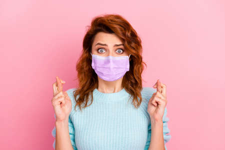 Portrait of lovely scared girl worrying showing crossed fingers wear mask isolated over pink pastel color backgroundの写真素材