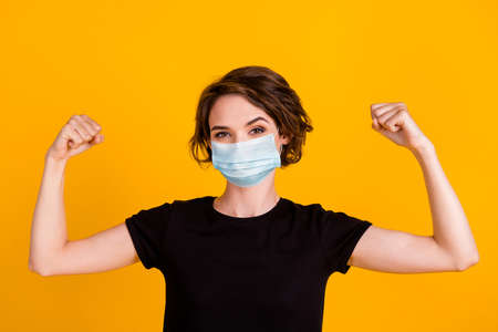 Close up portrait of attractive strong girl demonstrating muscles wear facial mask isolated yellow color backgroundの写真素材