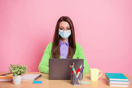 Portrait of focused girl sit table work remote laptop wear green shirt medical mask isolated pastel...