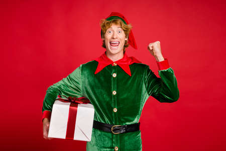 Photo of crazy helper elf hold box raise fist astonished wear green x-mas costume headwear isolated...