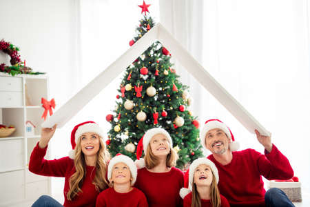 Portrait photo of lovely parents brother sisters spending time celebrating winter holidays wearing red headwear and warm jumpers sitting on xmas tree backgroundの写真素材
