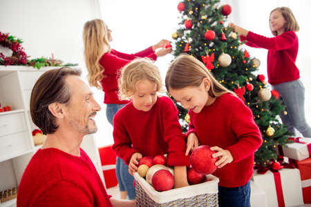 Photo of full big family five people gathering three small kids decorate x-mas tree dad bring balls daughter choose best wear red jumper jeans in home living room mistletoe indoorsの写真素材
