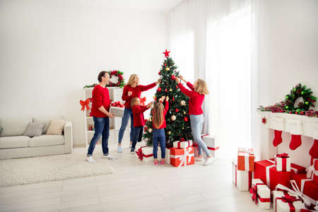 Photo of full big family five people meeting three little kids decorate x-mas tree dad help bring basket baubles garland wear red jumper jeans in home living room many gift box indoorsの写真素材