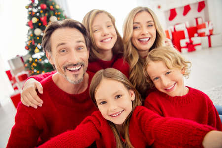 Closeup selfie photo of full big family five people meeting three little kids embrace toothy beaming smiling wear red jumper in living room x-mas tree garland gift boxes indoorsの写真素材