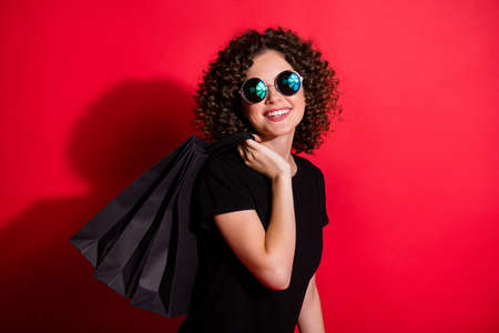 Photo of adorable cute curly woman wear casual black outfit eyeglasses holding bags back isolated red color backgroundの写真素材